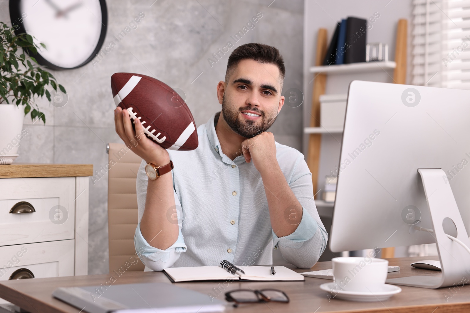 Photo of Young man with american football ball at table in office