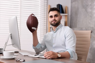 Young man with american football ball at table in office