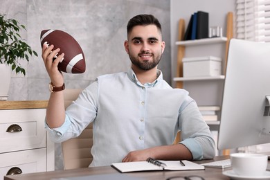 Young man with american football ball at table in office