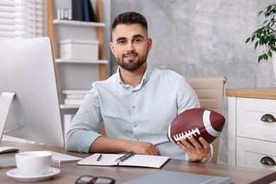 Photo of Young man with american football ball at table in office