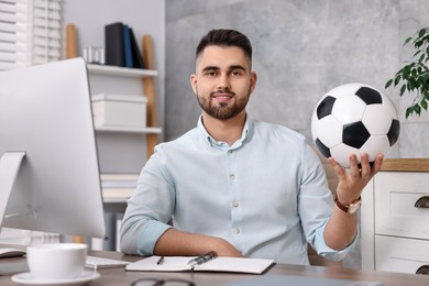 Young man with soccer ball at table in office