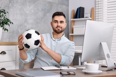 Young man with soccer ball at table in office