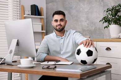 Young man with soccer ball at table in office