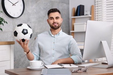 Photo of Young man with soccer ball at table in office