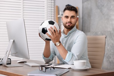 Photo of Young man with soccer ball at table in office