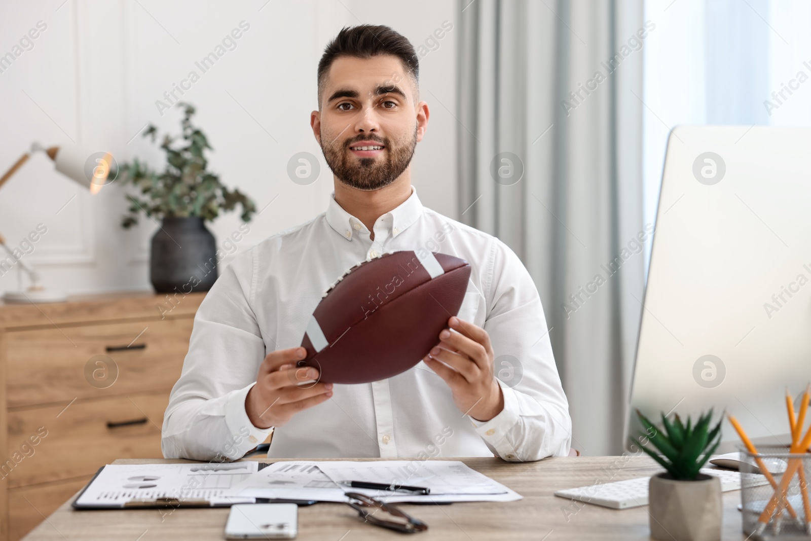 Photo of Young man with american football ball at table in office