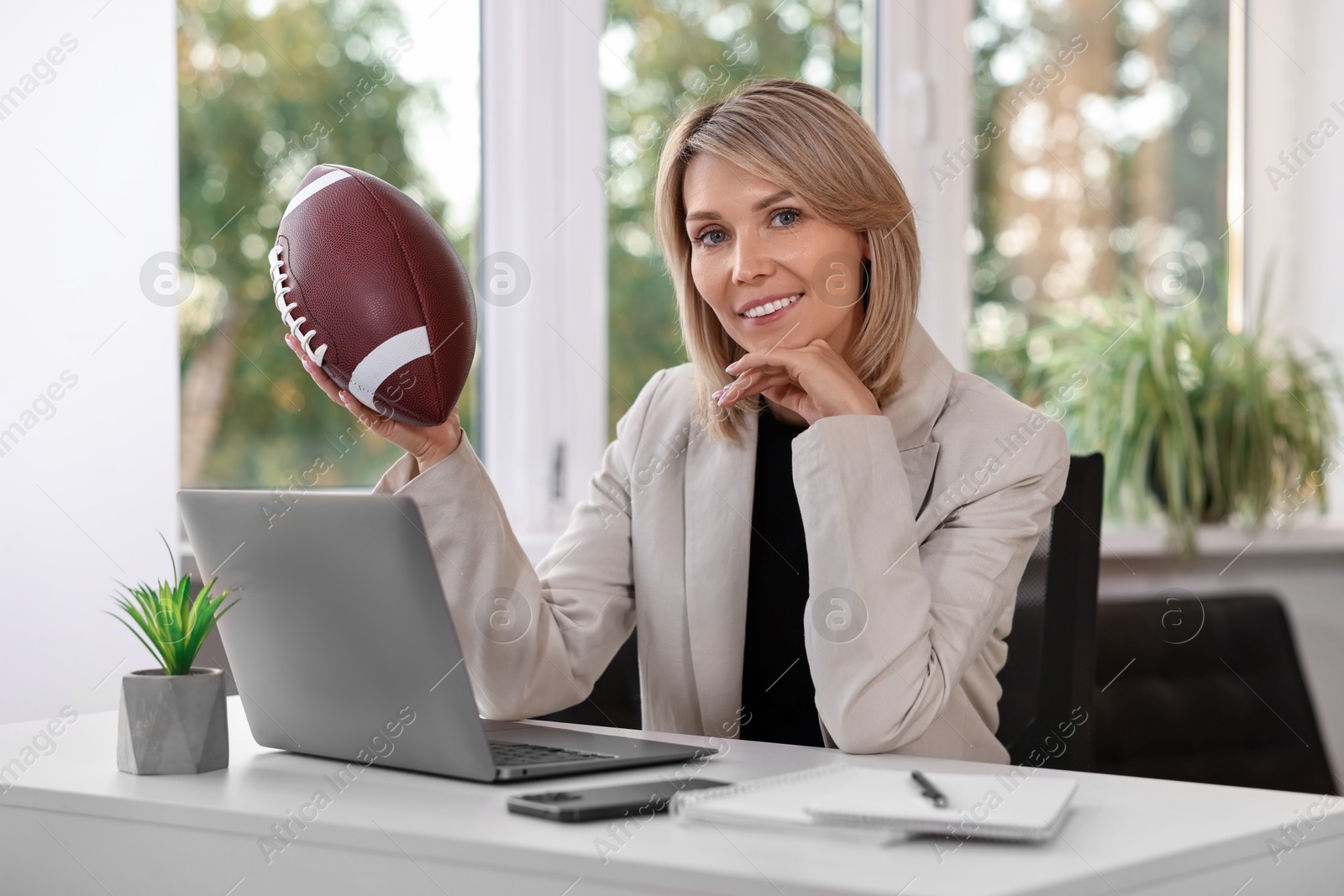 Photo of Smiling woman with american football ball at table in office