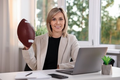 Photo of Smiling woman with american football ball at table in office
