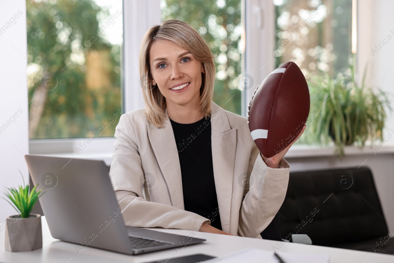 Photo of Smiling woman with american football ball at table in office