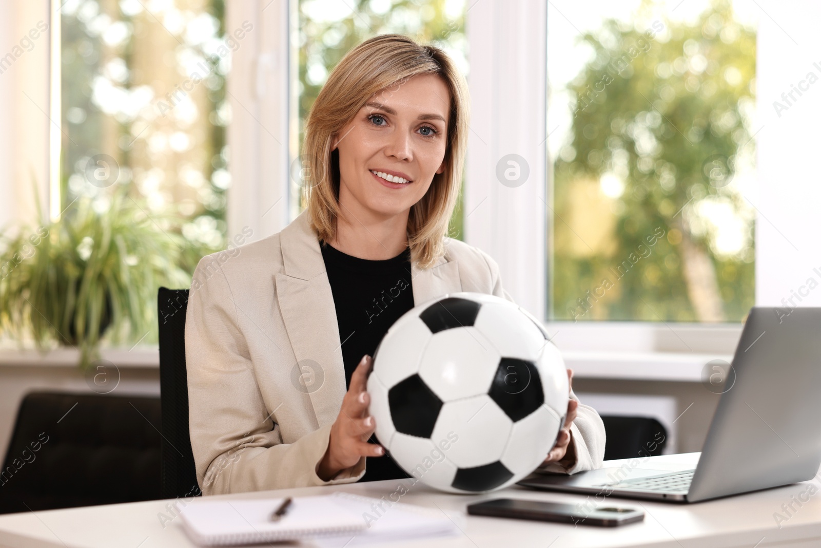 Photo of Smiling woman with soccer ball at table in office