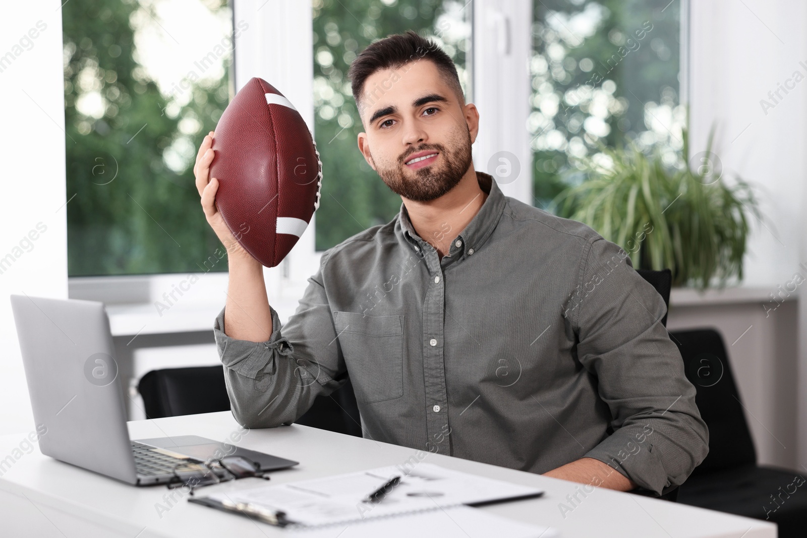 Photo of Young man with american football ball at table in office