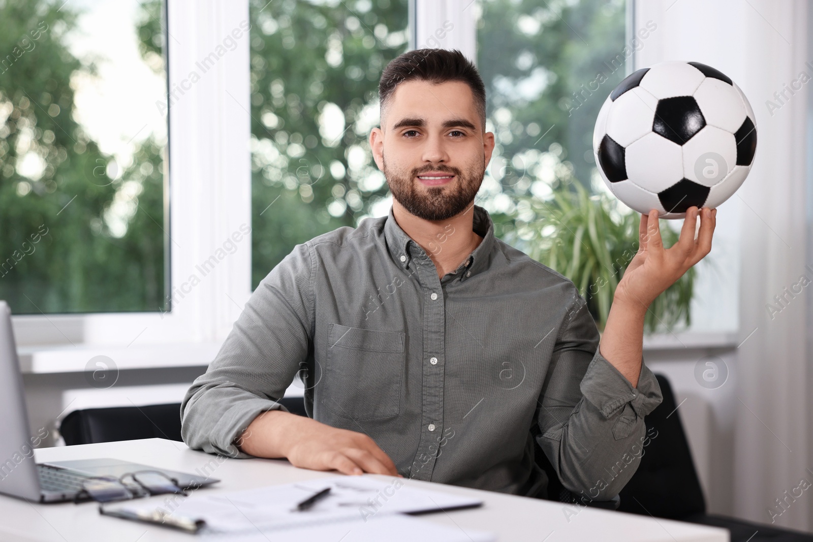 Photo of Young man with soccer ball at table in office