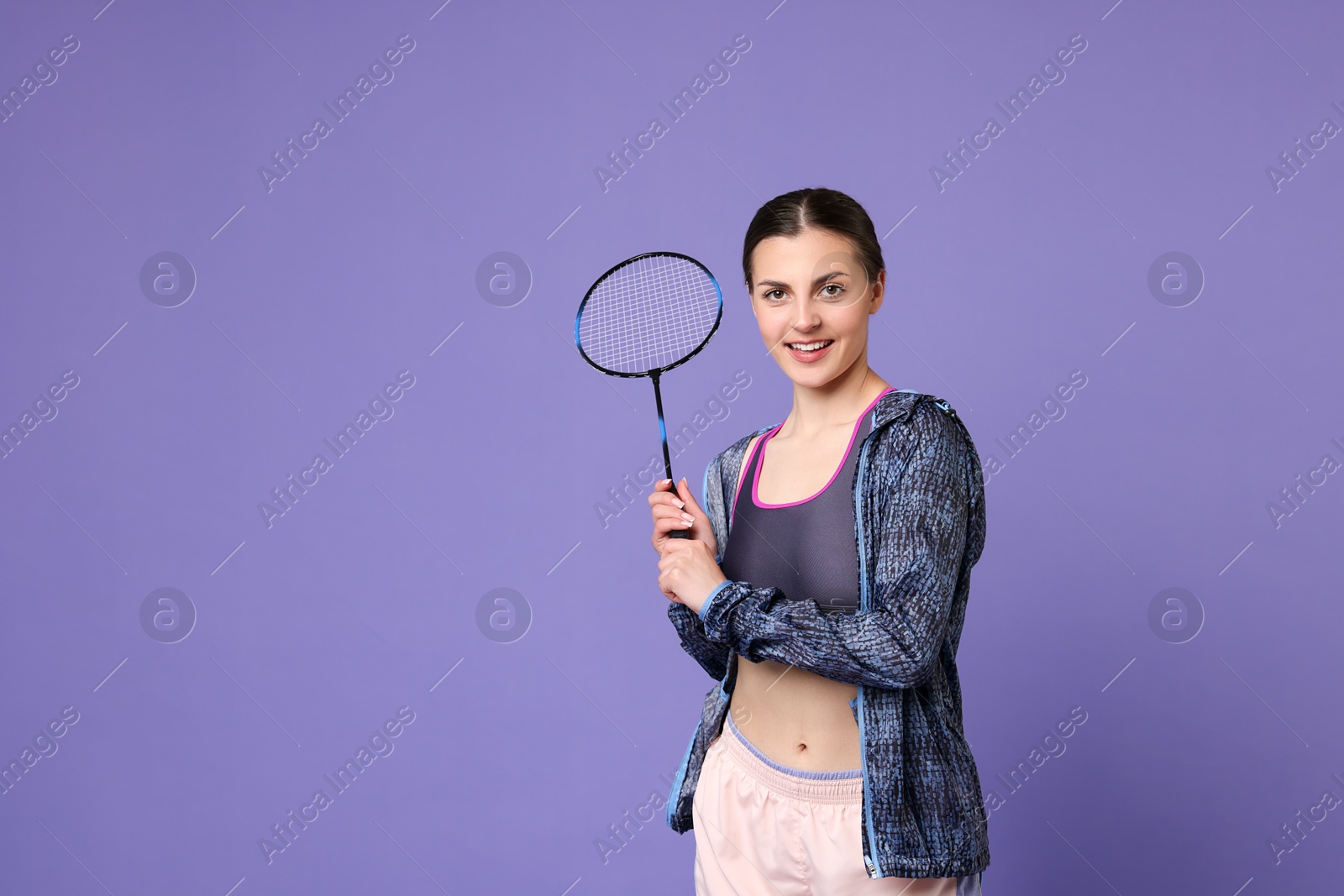 Photo of Young woman with badminton racket on purple background, space for text