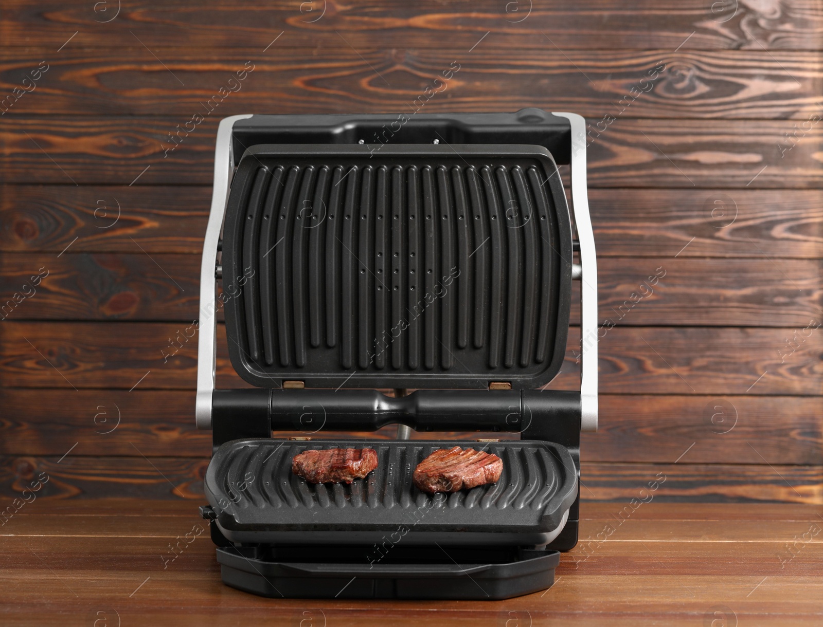 Photo of Electric grill with tasty meat steaks on wooden table