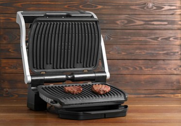 Photo of Electric grill with tasty meat steaks on wooden table. Space for text