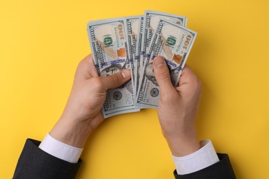 Photo of Money exchange. Man holding dollar banknotes on yellow background, top view