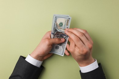 Photo of Money exchange. Man holding dollar banknotes on olive background, top view