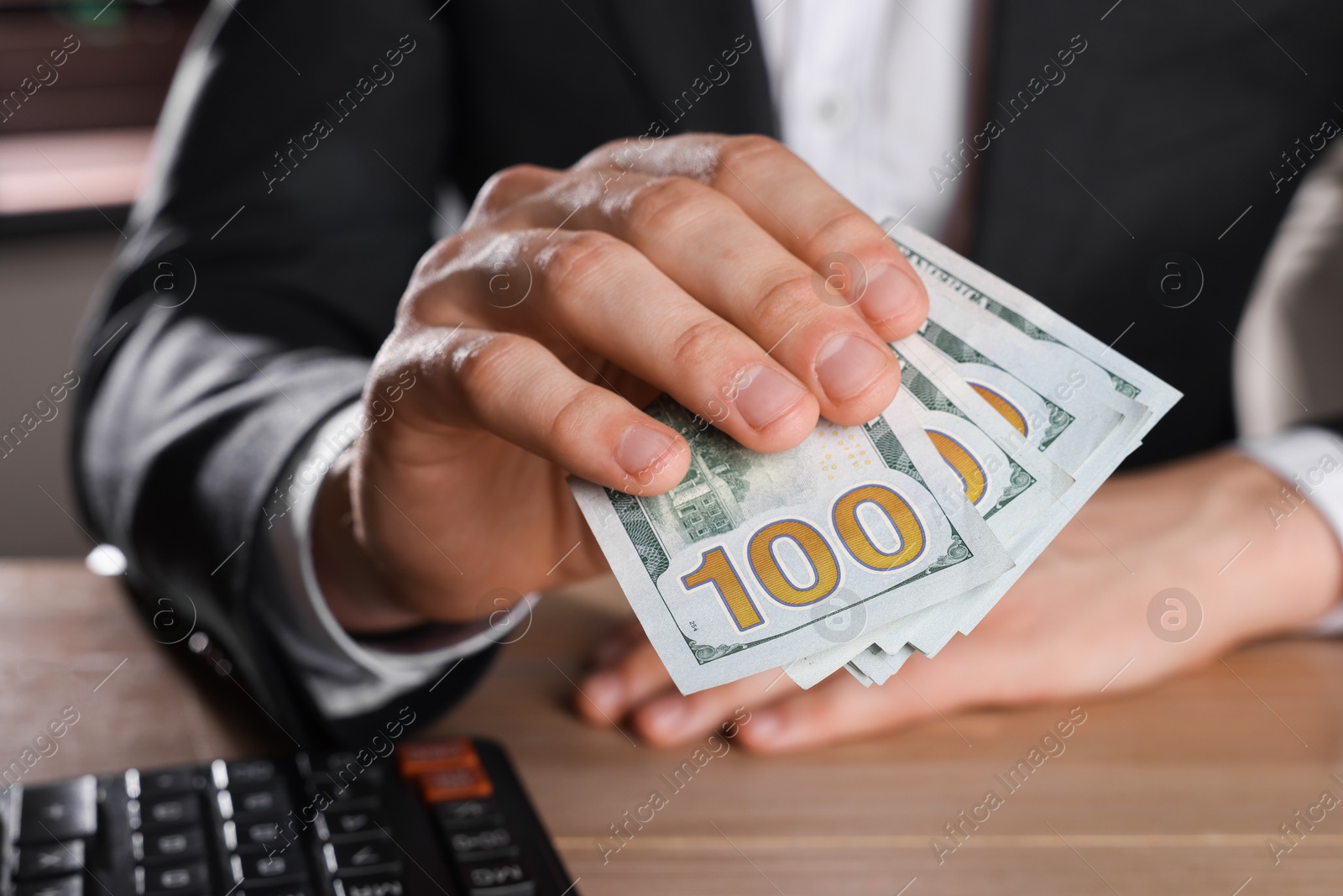 Photo of Money exchange. Man holding dollar banknotes at wooden table, closeup