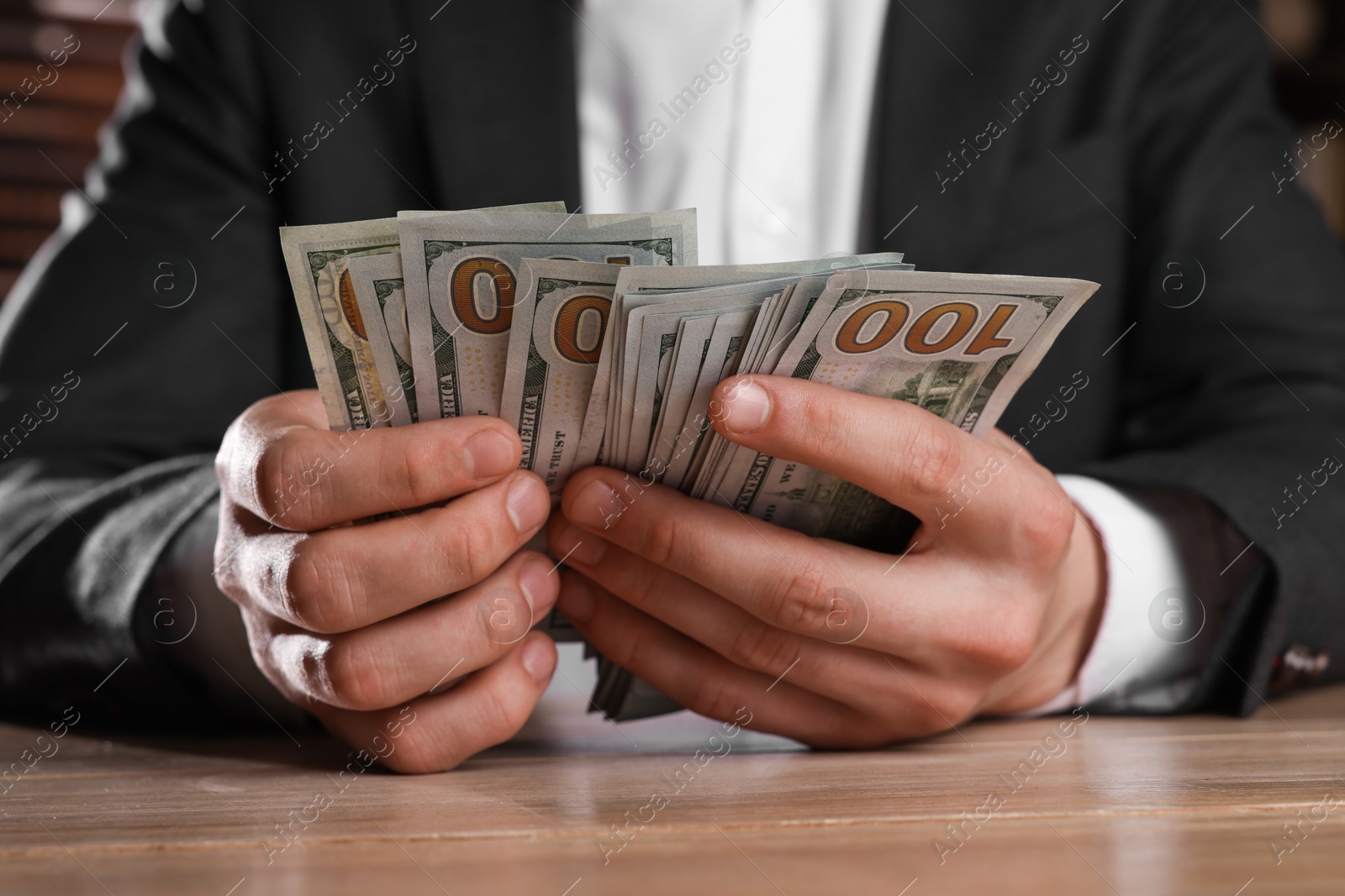 Photo of Money exchange. Man counting dollar banknotes at wooden table, closeup