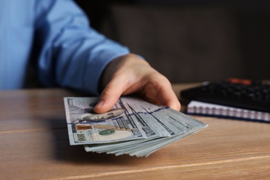 Photo of Money exchange. Woman holding dollar banknotes at wooden table, closeup