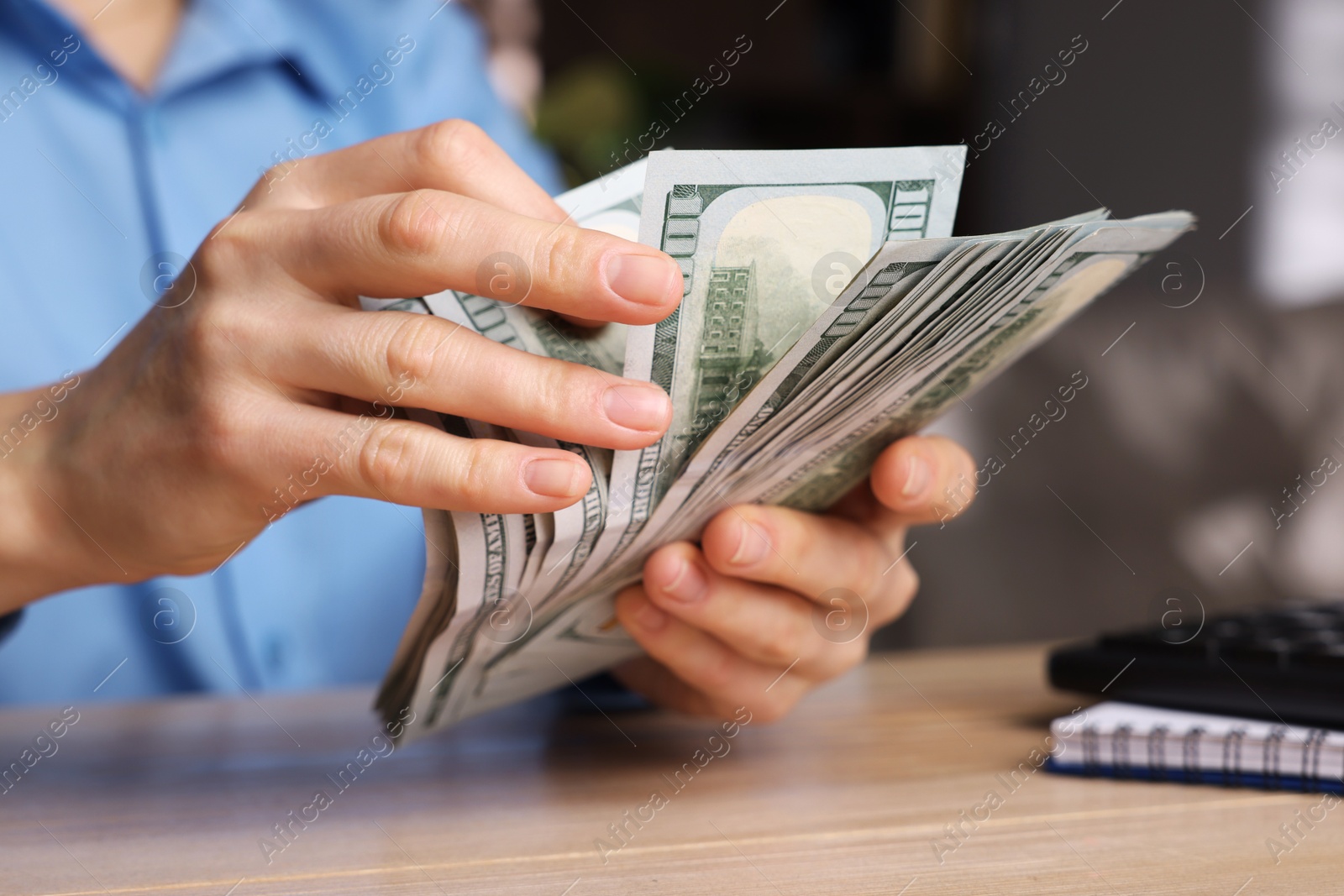 Photo of Money exchange. Woman counting dollar banknotes at wooden table, closeup