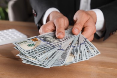 Money exchange. Man counting dollar banknotes at wooden table, closeup