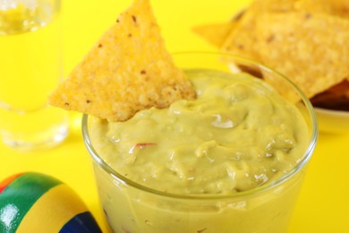 Delicious guacamole with nachos chip on yellow background, closeup