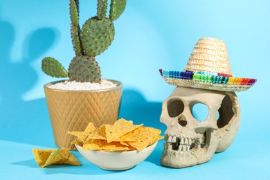Photo of Human scull with Mexican sombrero hat, cactus and nachos chips on light blue background