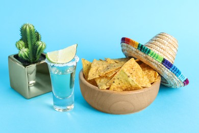 Mexican sombrero hat, cactus, nachos chips and tequila on light blue background