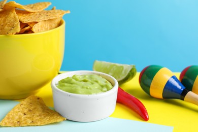 Photo of Delicious guacamole with nachos chips, chili pepper, lime and maracas on color background