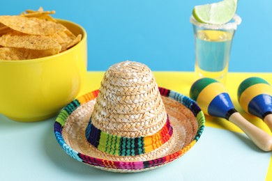 Photo of Mexican sombrero hat, nachos chips, maracas and tequila on color background