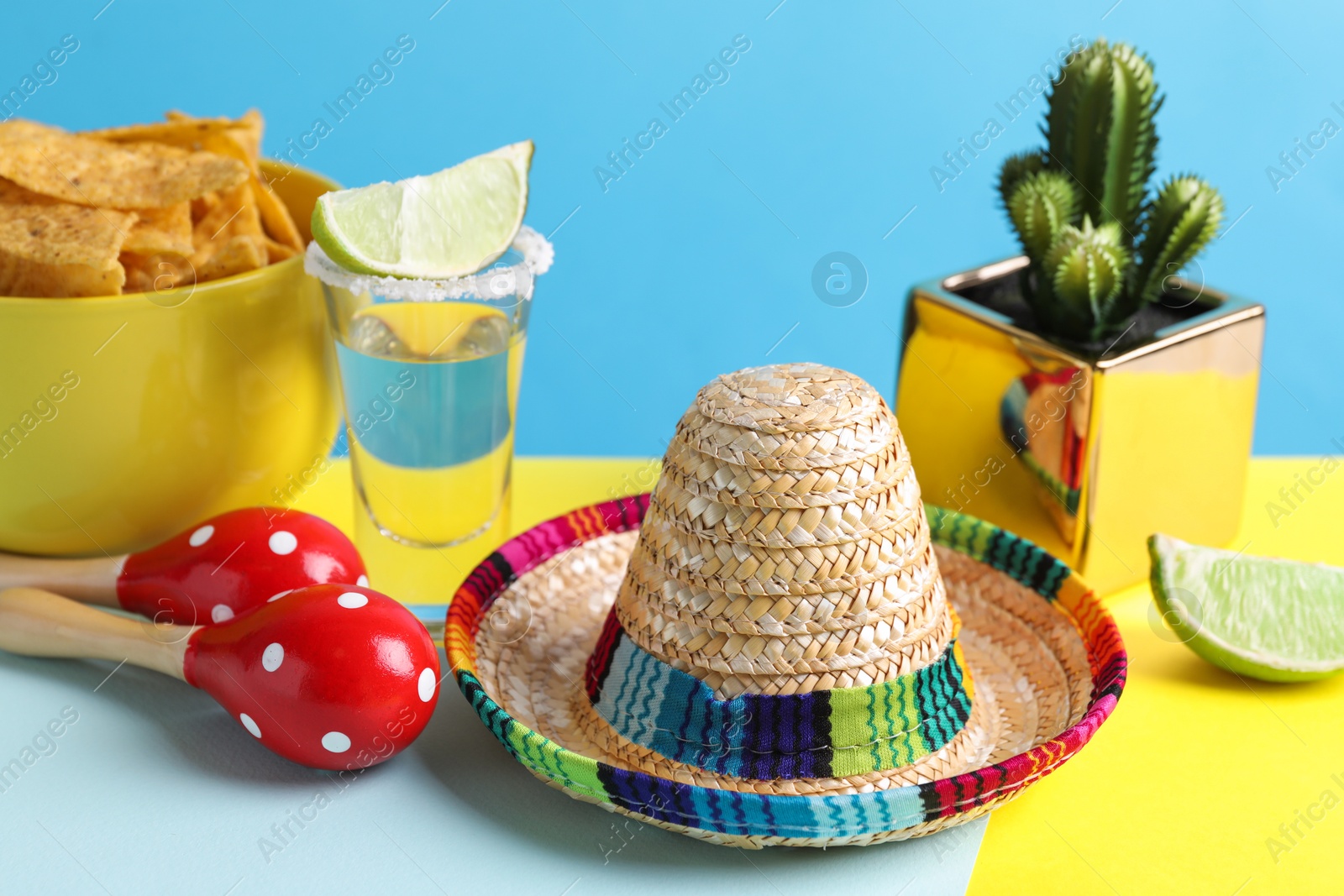 Photo of Mexican sombrero hat, cactus, nachos chips, maracas and tequila on light blue background