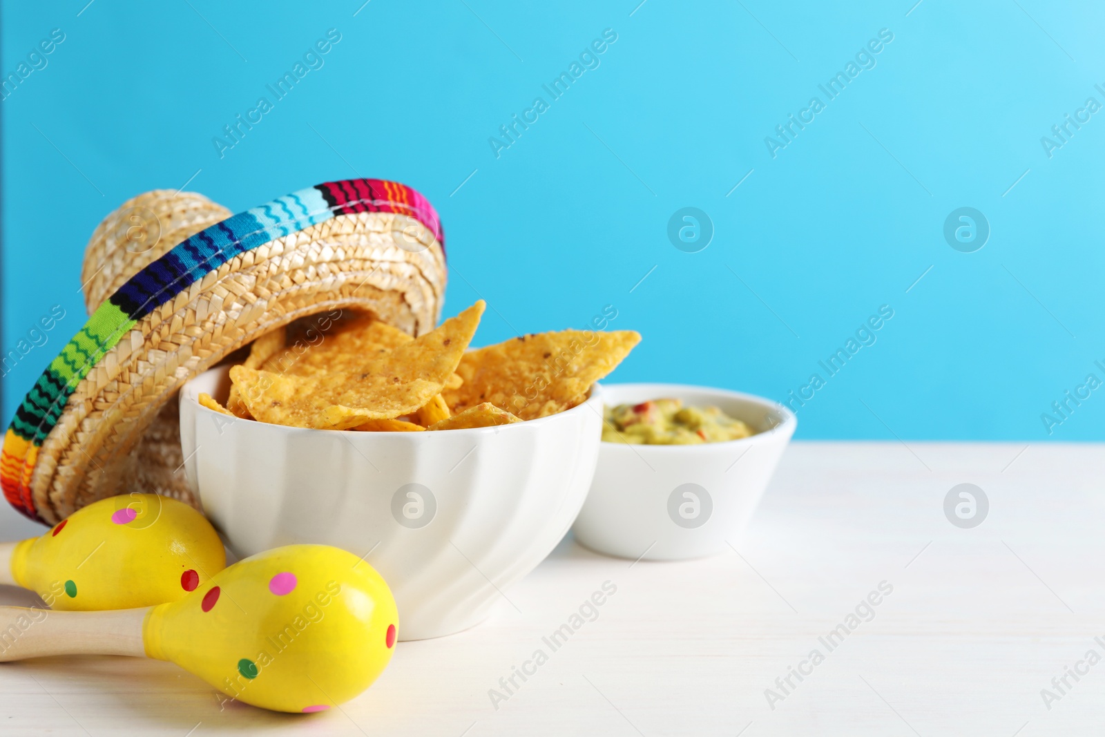 Photo of Mexican sombrero hat, nachos chips, guacamole and maracas on white wooden table. Space for text