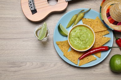 Guacamole, nachos chips, tequila, Mexican sombrero hat and ukulele on wooden table, flat lay. Space for text