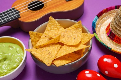 Photo of Nachos chips, maracas, guacamole, Mexican sombrero hat and ukulele on purple background