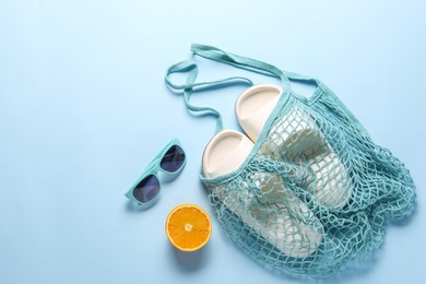 String bag, sunglasses, orange and slippers on light blue background, top view. Space for text