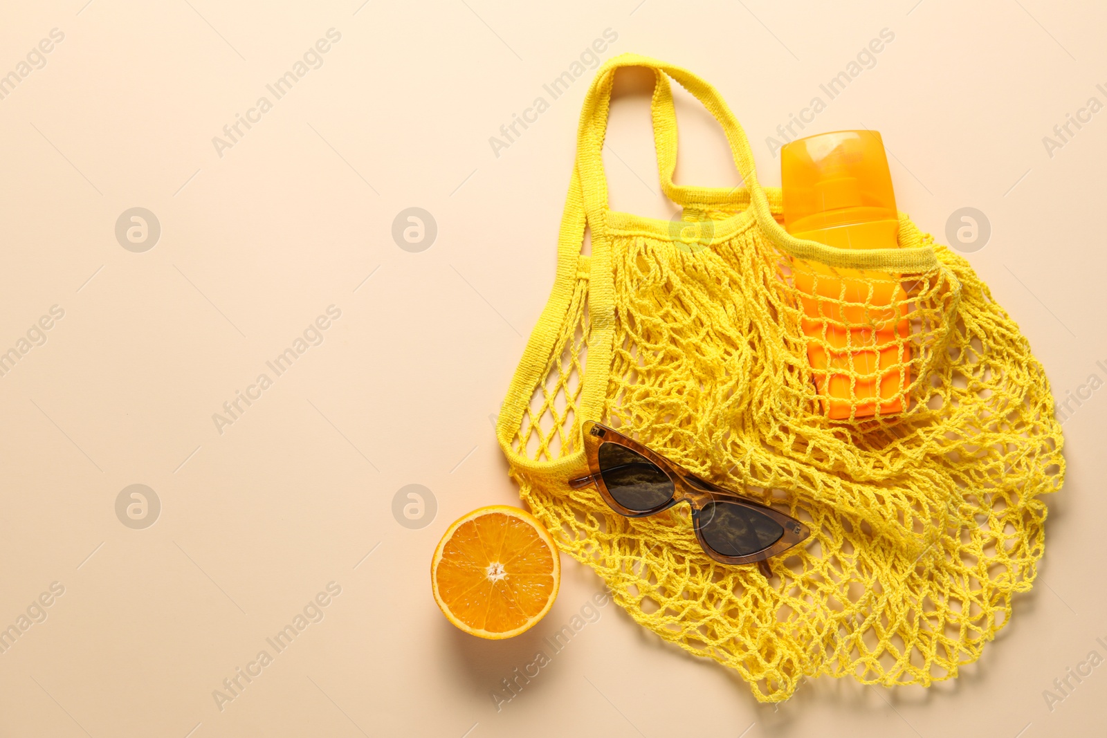 Photo of String bag, sunglasses, orange and sunscreen on beige background, top view. Space for text