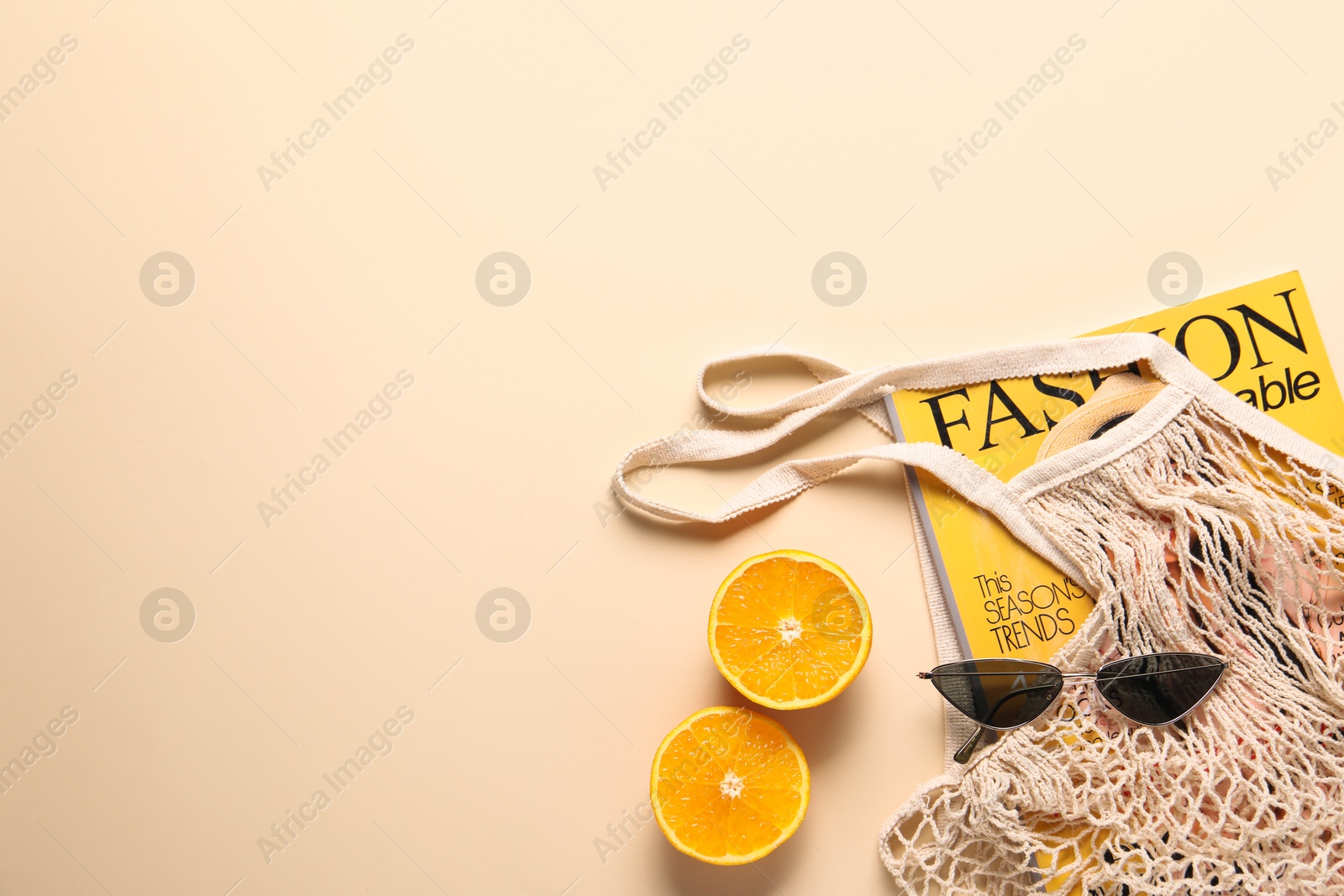 Photo of String bag, magazine, sunglasses and halves of orange on beige background, top view. Space for text