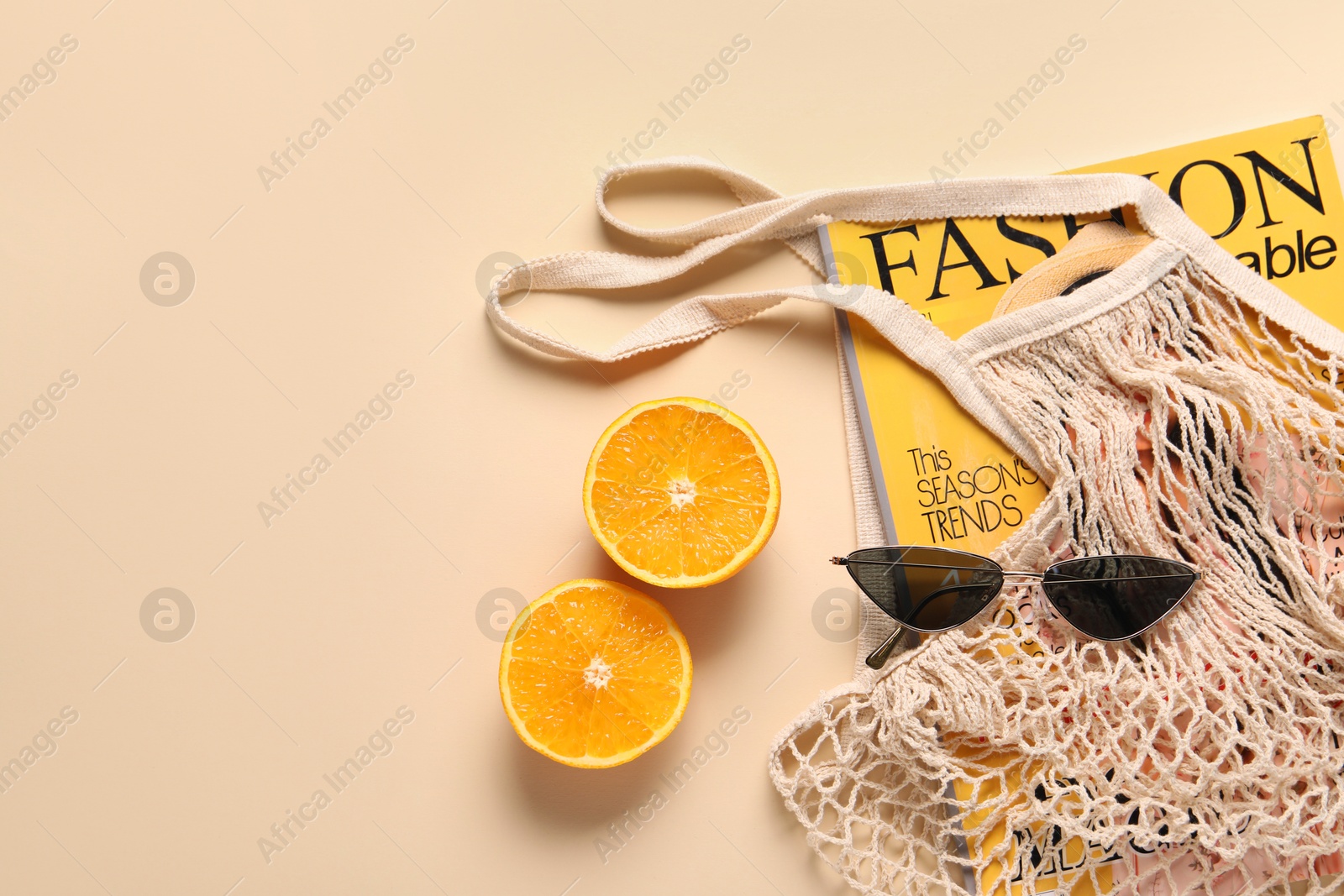 Photo of String bag, magazine, sunglasses and halves of orange on beige background, top view. Space for text