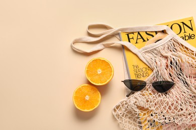 Photo of String bag, magazine, sunglasses and halves of orange on beige background, top view. Space for text