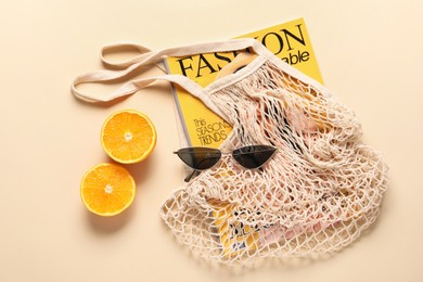 String bag, magazine, sunglasses and halves of orange on beige background, top view