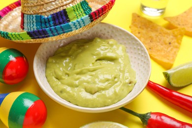 Photo of Guacamole, Mexican sombrero hat, nachos chips, maracas and chili pepper on yellow background, closeup