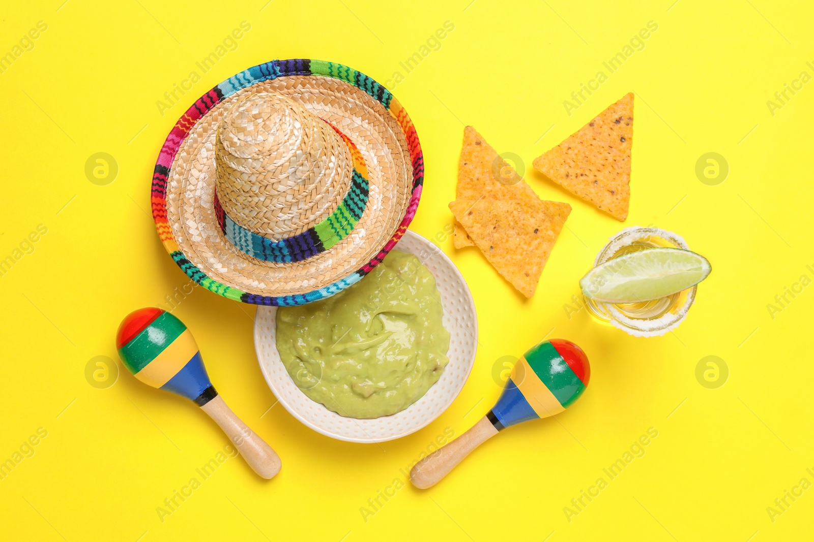 Photo of Mexican sombrero hat, tequila, nachos chips, guacamole and maracas on yellow background, flat lay