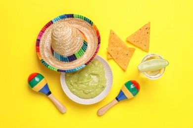 Mexican sombrero hat, tequila, nachos chips, guacamole and maracas on yellow background, flat lay