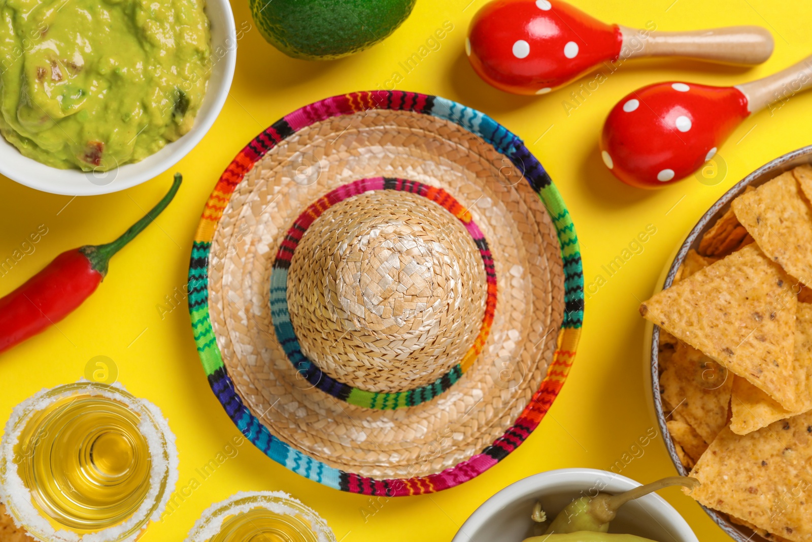 Photo of Mexican sombrero hat, tequila, nachos chips, guacamole and maracas on yellow background, flat lay