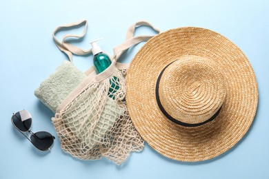 String bag, sunglasses, towel, straw hat and cosmetic product on light blue background, top view