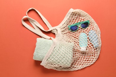 String bag, sunglasses, cosmetic products and towel on coral background, top view