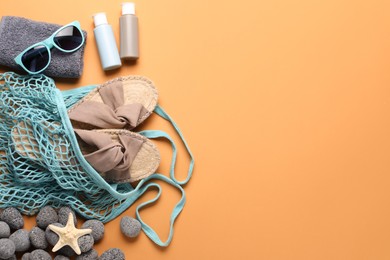 String bag and different beach accessories on pale orange background, flat lay. Space for text