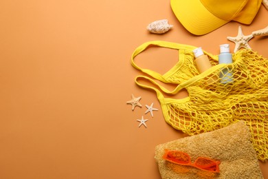 String bag and different beach accessories on pale orange background, flat lay. Space for text