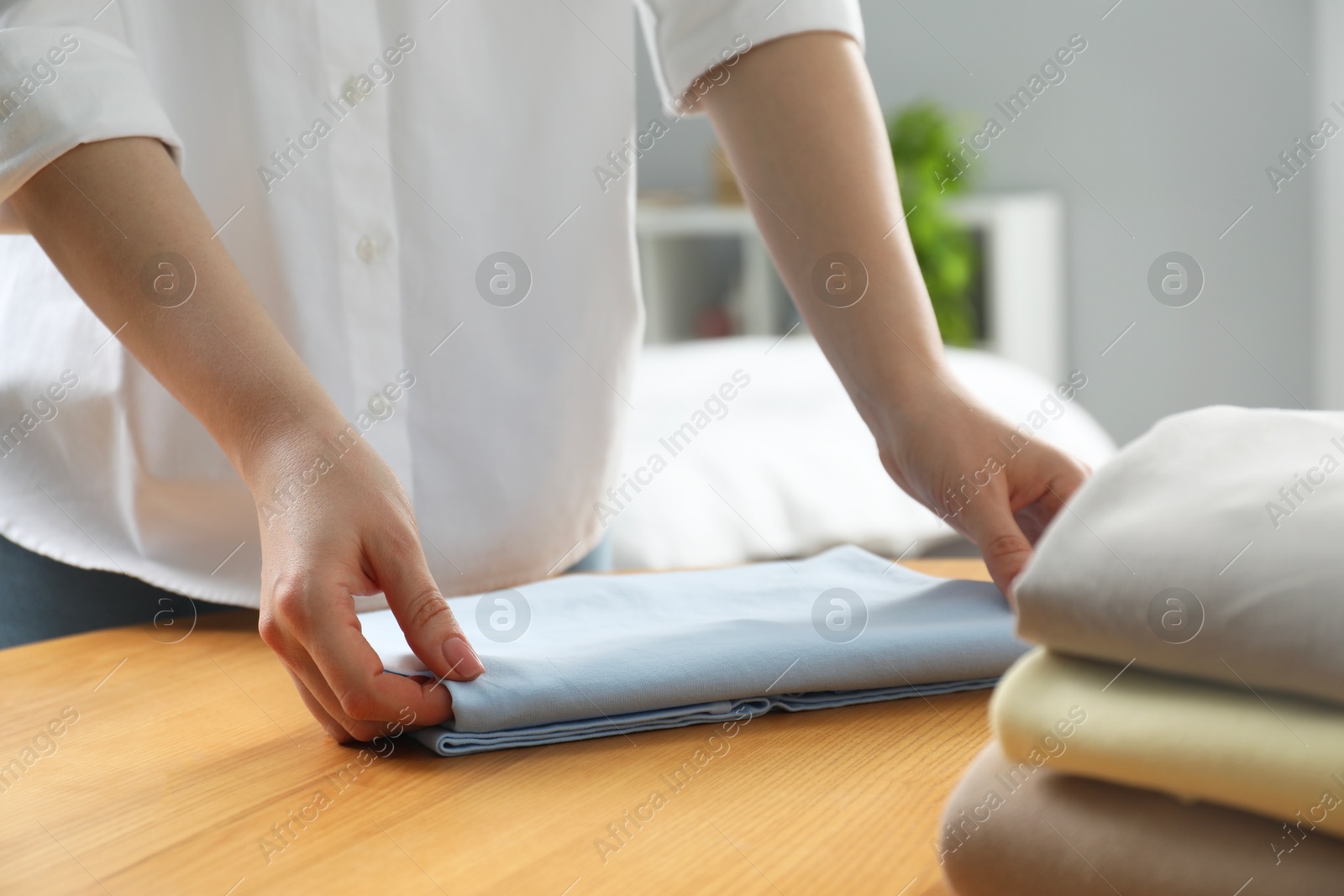 Photo of Woman folding clothes at wooden table indoors, closeup